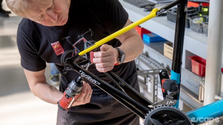 A technician assembles a Wilier bike, attaching a brake caliper to a rear mount with an impact wrench.